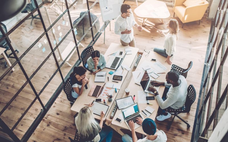 Top view of multiracial young creative people in modern office. Group of young business people are working together with laptop, tablet, smart phone, notebook. Successful hipster team in coworking. Freelancers.